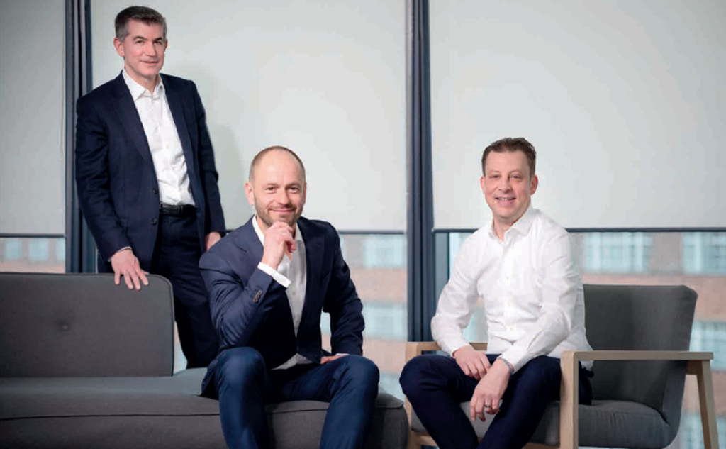 Three men in business attire pose thoughtfully in a modern office space.