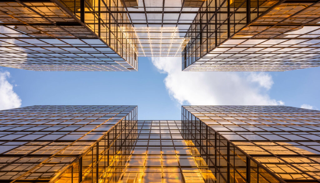 View from below of glass buildings creating a geometric frame against a blue sky.