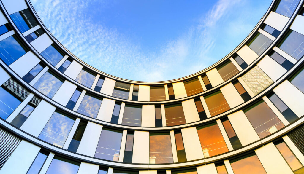 Low angle of a modern, curved building reflecting the blue sky and clouds.