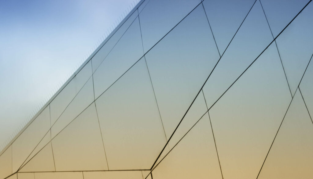 Modern building facade with intersecting glass panels in front of a gradient sky.