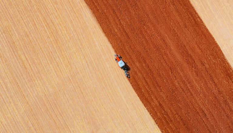 Aerial view of a farmer plowing contrasting fields of light tan and brown.