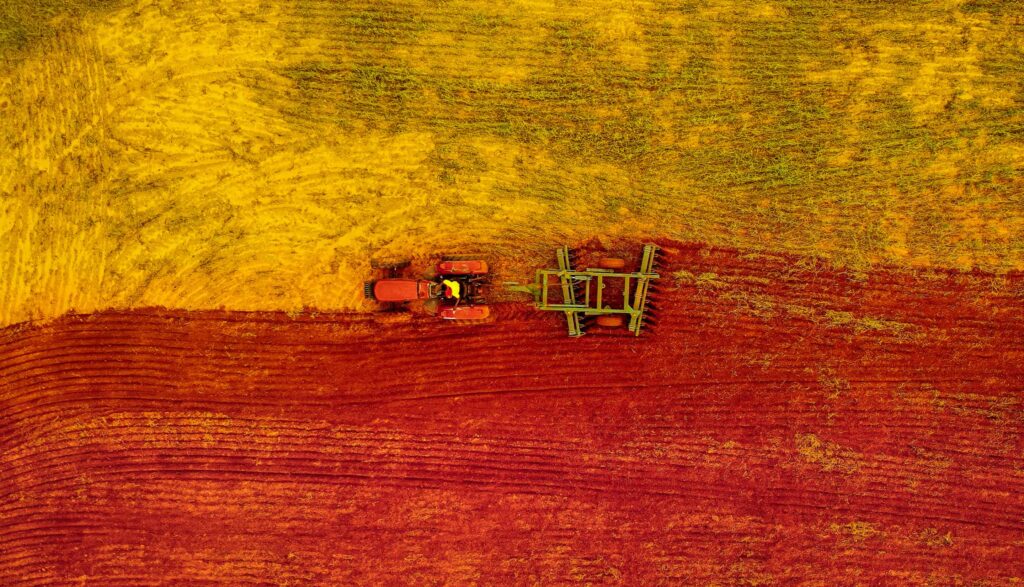 Aerial view of tractor plowing on a yellow and red field.