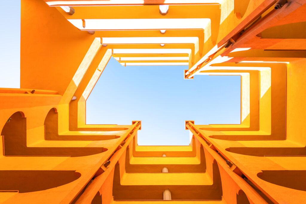 Geometric view of orange architectural walls converging towards a blue sky.