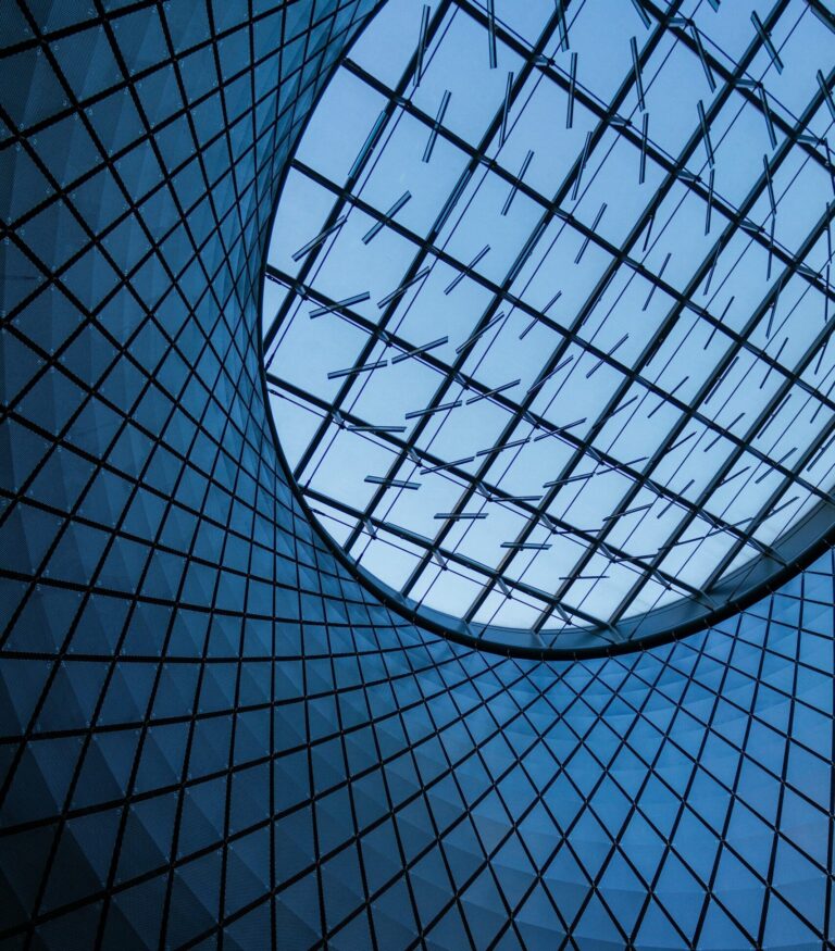 Geometric glass ceiling with a circle opening showcasing a blue sky.
